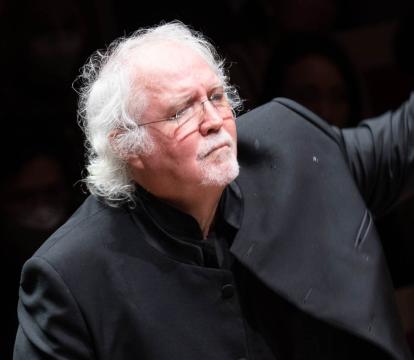 Donald Runnicles stands with his left hand raised as he conducts an orchestra