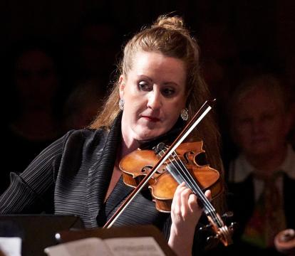 A female violinist plays the violin in front of a Chamber Orchestra