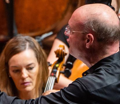 Stephen Layton conducts an Orchestra with arms outstretched