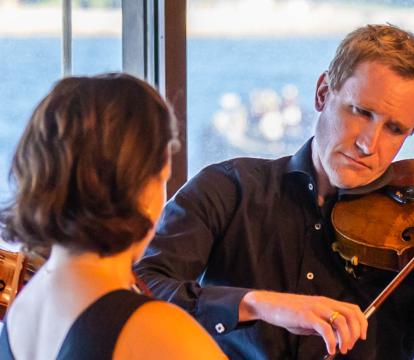 Three violin players stand playing the violin in the Sydney Opera House Utzon Room