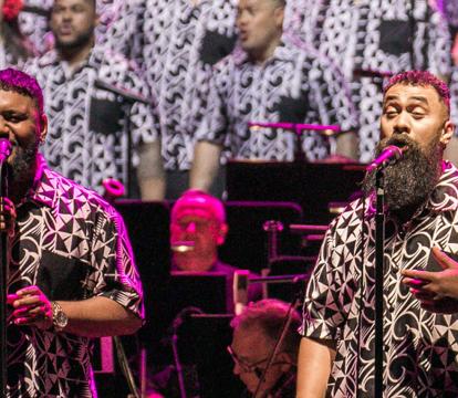 The Signature Choir in matching black and white designed shirts sing in front of an orchestra