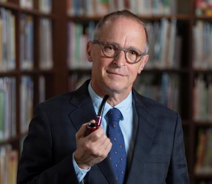 David Sedaris an American humorist in a suit holding a cigar pipe.