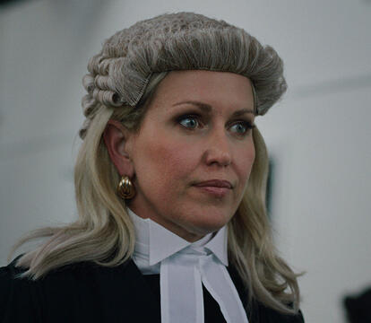 A woman wearing a traditional barrister's wig and a black gown, with an elegant white collar and large earrings.