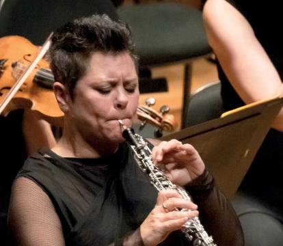 A woman with short hair playing flute in an orchestra.