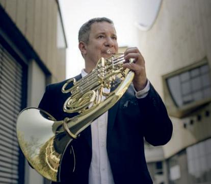 A man in blue suit jacket playing a trumpet.