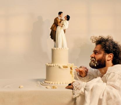 A bearded man picks away and glares at a wedding cake with a happy couple in period costume at the top.