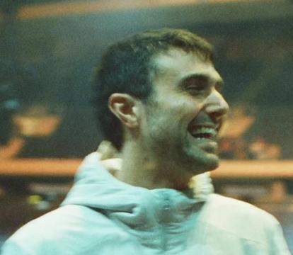A white man in a white jacket looks over his shoulder smiling