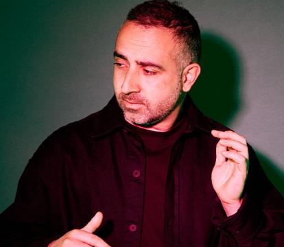 A middle aged man in a black jacket standing in dark studio lighting.