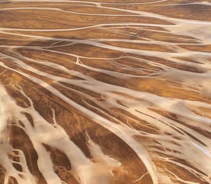 A very wide bird's eye view of empty brown arid land with river systems zip zagging through the land