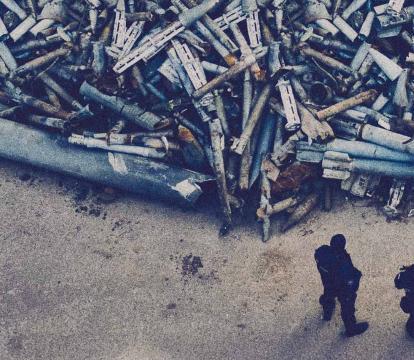 Two soldiers stand in front of a pile of discarded missiles.