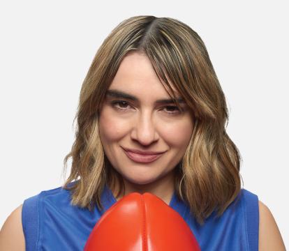 A woman with light brown shoulder length hair wearing a blue sleeveless jersey and holding a red football.
