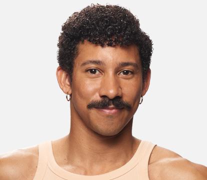 A headshot of a man with curly dark hair, wearing a peach coloured singlet against a light grey background.