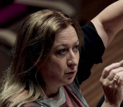 A blonde woman holding a conductor baton.
