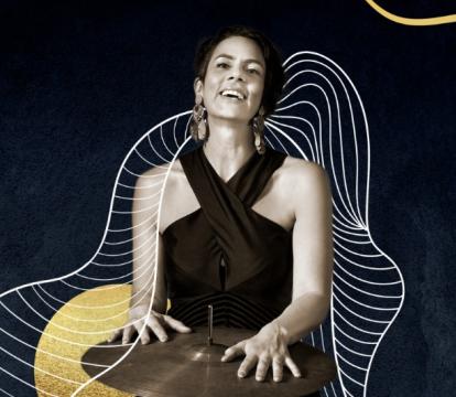 A woman in black dress standing with her hands on a crash cymbal.