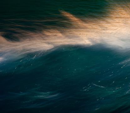 The surface of a dark body of water with light reflected of gentle waves and wind creating soft spray of whitewater.
