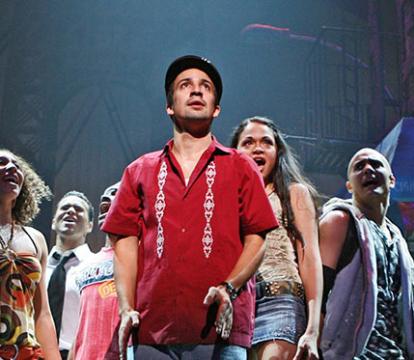 A group of people in colorful clothes, standing and singing on stage.