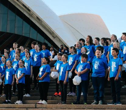 A group of people wearing blue stand on the steps of the Sydney Opera House.