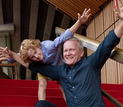 A man and a boy sitting on red stairs with their arms open.