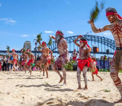 Men in sand pit performing indigenous dance in the homeground of Sydney opera house.