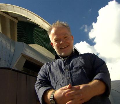 A man in blue shirt in front of Sydney opera house.