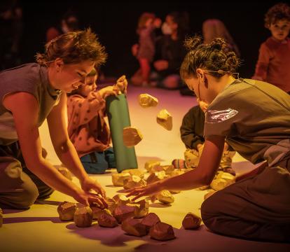 Artists and children explore building blocks on the floor.