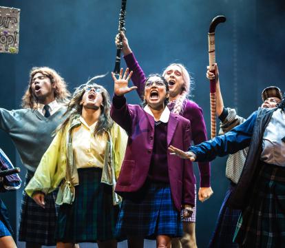 A group of girls with hockey sticks dancing on stage.