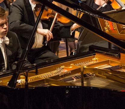 A man playing a grand piano in an orchestra.