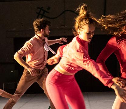 Five dancers wear pink and stand in a diagonal line caught in movement.