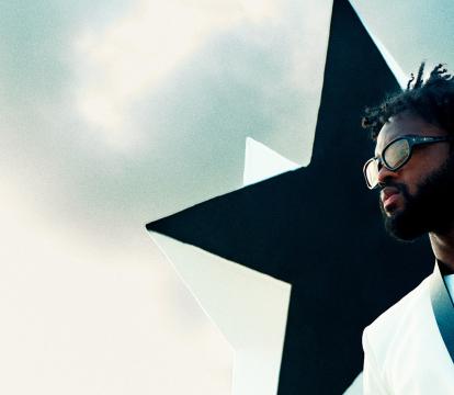 A young black man wears sunglasses and poses in front of a large black star.