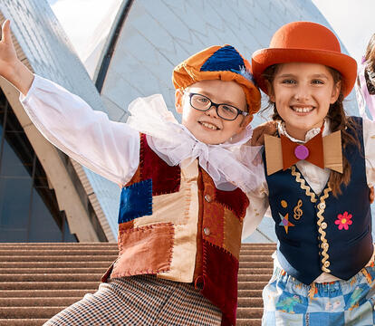 Three children stand in front of the Sydney Opera House smiling.