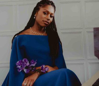 Isata Kanneh-Mason pictured in front of a grand piano in a blue dress.