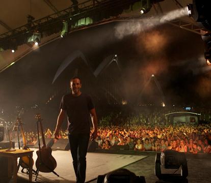 Backstage view of a man smiling on stage in front of a lively audience.