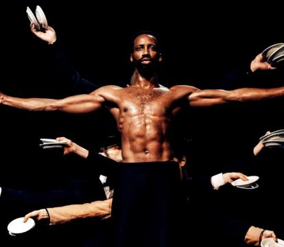 A topless man holding plates, surrounded by a bunch of hands holding plates.