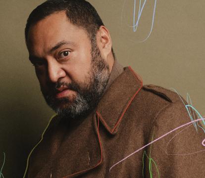 A man wearing a brown wool coat looking sidelong against a olive green background with subtle scribbled marks in pink, red, light blue and green.