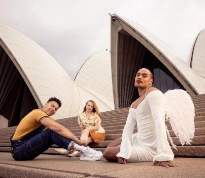 Three individuals sitting outside on the stairs of Sydney opera house.