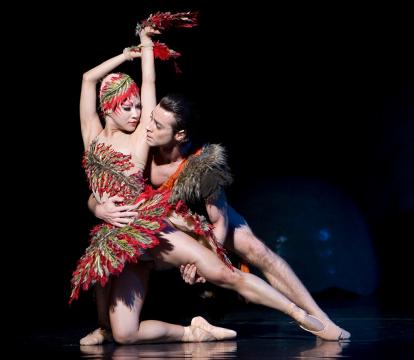 Two dancers, one in a red feathered costume.