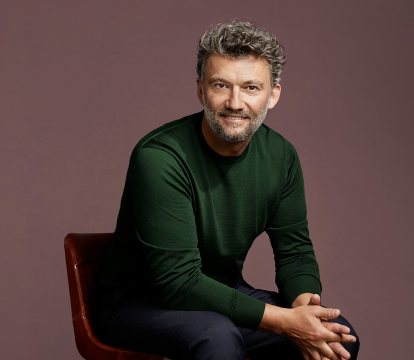 A man with grey hairs in green sweater sitting on the chair.