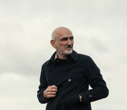 A man with grey hair in a black coat standing outside.