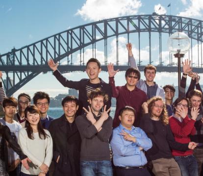 A group of people standing near Sydney opera house with Harbour bridge in the background.