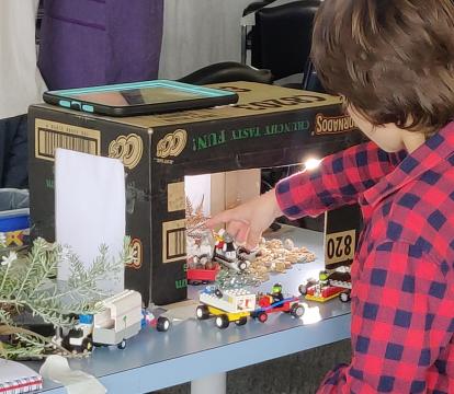 A young boy moving toy cars within a cardboard box