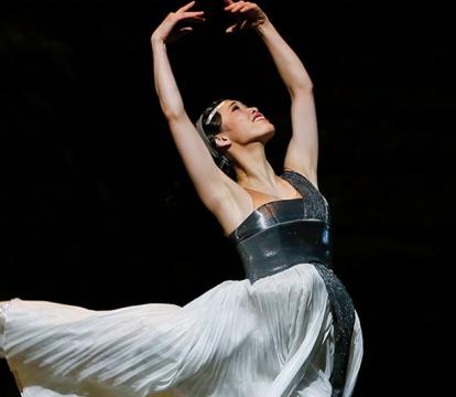 A woman in a white dress leaping with her hands above her head.