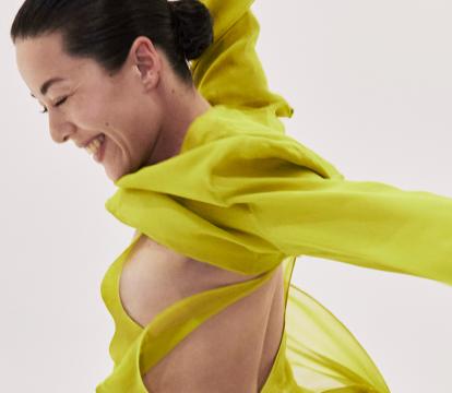 A dancer in bright yellow, in motion against a light grey background.