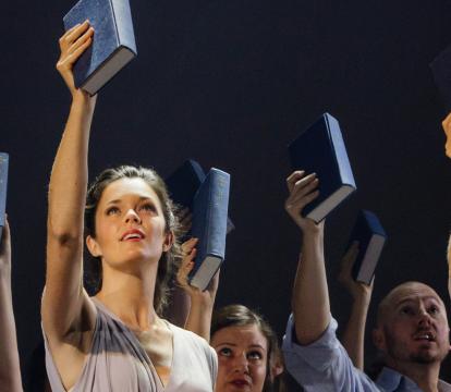 The cast wears neutral outfits, all holding up a book in their right hand