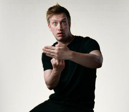 Daniel Sloss a comedian hiding his hand with another hand in front of it.