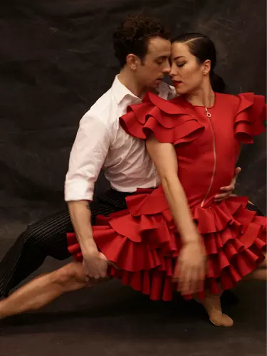 A man with dark hair in a white shirt holds a woman with dark hair in a red dress around the wait with his hand on her leg.