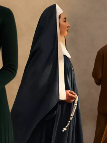 A woman dressed as a nun faces the right. Another woman wearing black holds a candle and a man faces the back wearing a copper coloured suit.