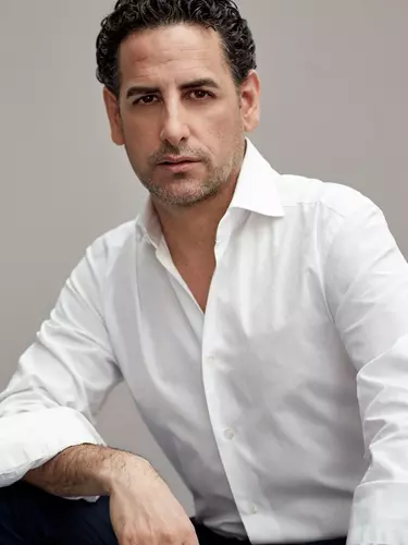 Man with dark curly hair looks at the camera wearing a white shirt