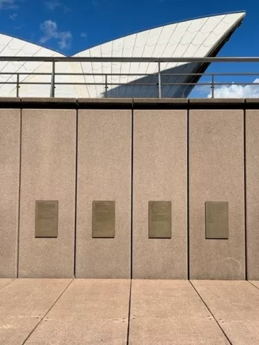 A wall with four plaques on it, with part of the Sydney Opera House in the background.