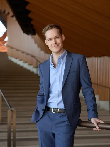 Harry Prouse wearing a blue suit, standing inside the Sydney Opera House.