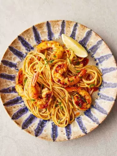 Spaghetti, prawns and a slice of lemon on a patterned plate, on a beige tabletop.